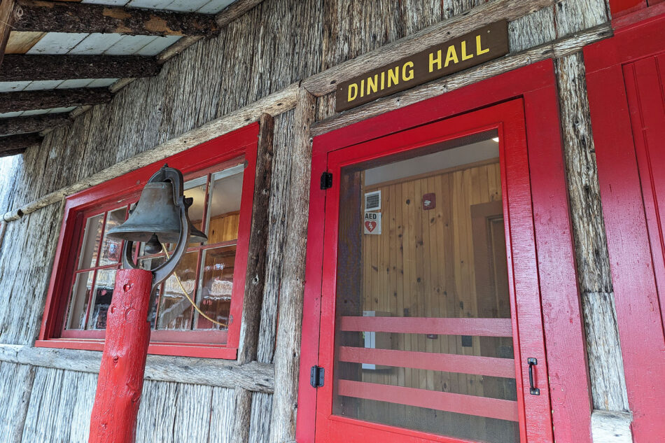 A detailed photograph the entrance sign and dinner bell outside the Dining Hall at Great Camp Sagamore.