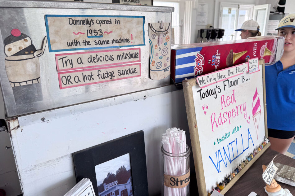 A handwritten sign at Donnelly's Soft Ice Cream announces the shop opened in 1953 with the same machine, alongside a chalkboard listing the day's flavor as red raspberry twisted with vanilla.