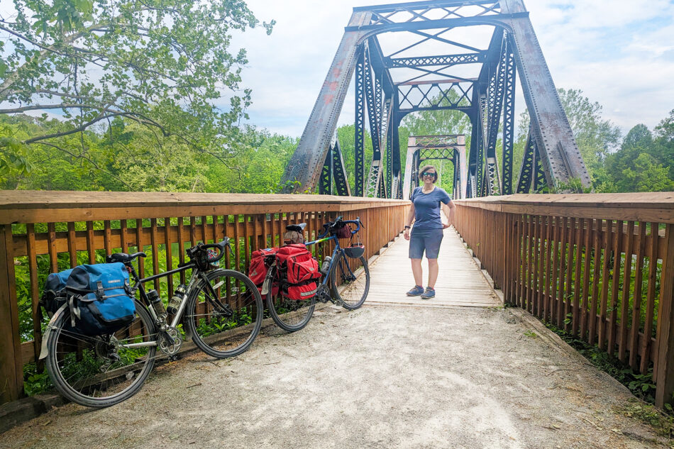 Dharma posing next two two bicycles in front of a historic metal bridge.