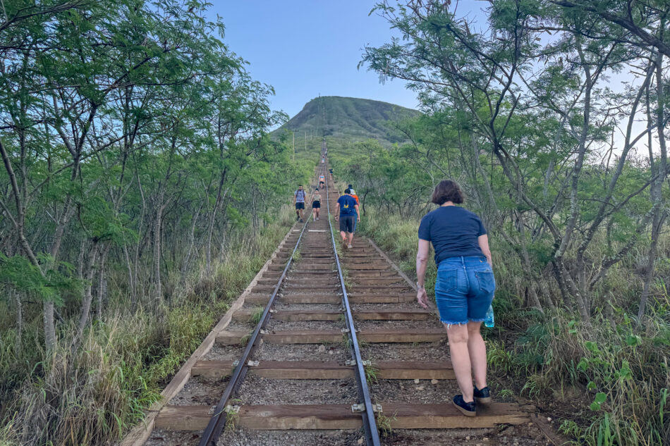 Hikers ascending the Koko Crater Trail, also known as the Koko Head Stairs, surrounded by lush greenery and railroad tracks leading up the steep incline.