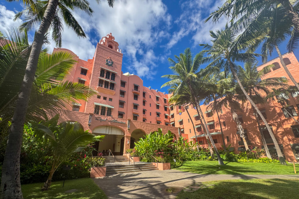 The Royal Hawaiian Hotel, also known as the 'Pink Palace of the Pacific,' surrounded by lush palm trees and tropical gardens under a vibrant blue sky.