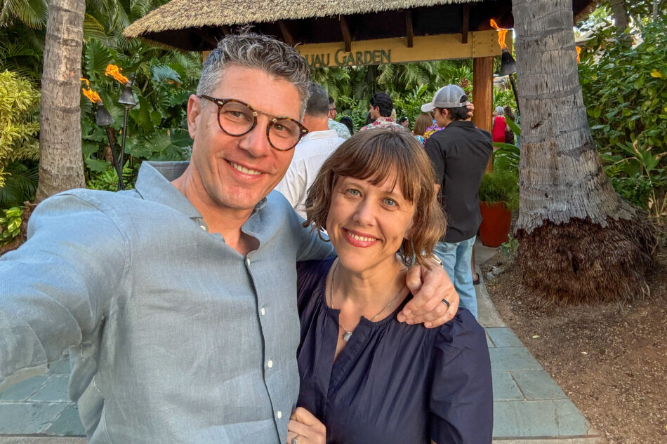 Dharma and I smiling in front of the Luau Garden entrance, surrounded by lush tropical greenery and tiki torches in the background.