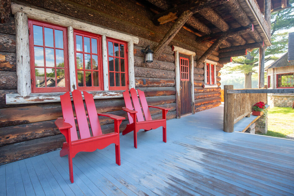 A view of red Adirondack chairs on the porch of the Main Lodge at Great Camp Sagamore.