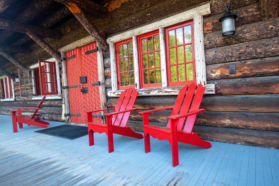 A view of the front doors and red Adirondack chairs on the porch of the Main Lodge at Great Camp Sagamore.