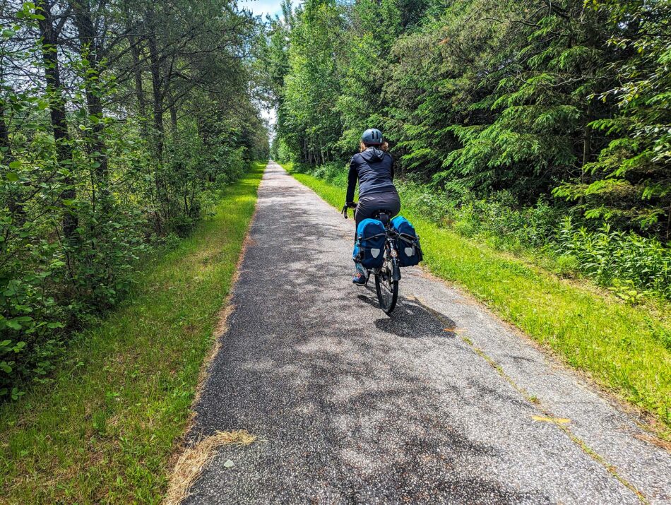 Dharma riding on the P'tit Train du Nord trail, surrounded by lush green trees and foliage on a sunny day.