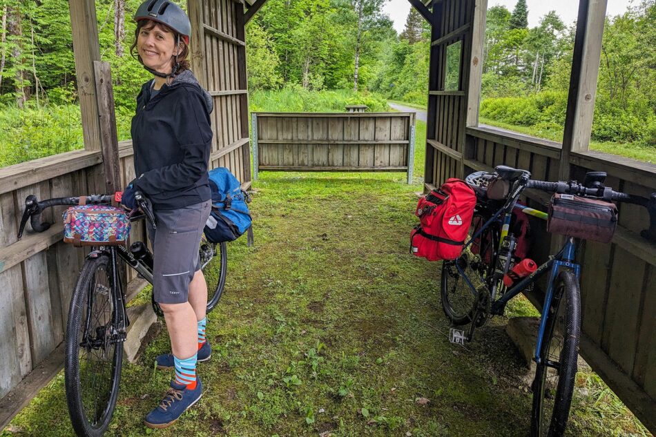 Dharma smiling standing next to a bike under a wooden shelter along the P'tit Train du Nord trail.