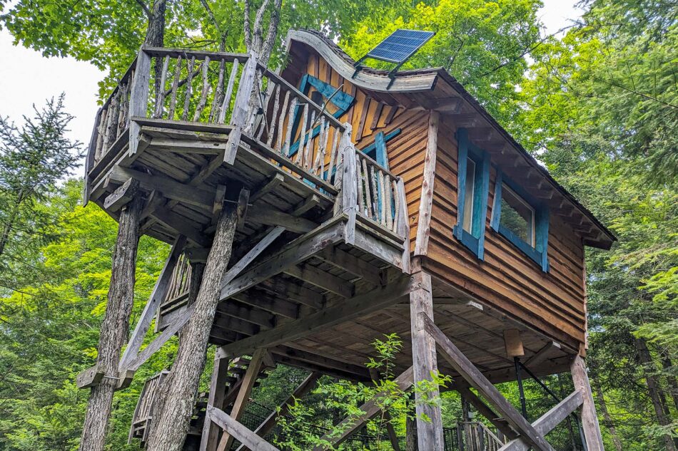 Wooden treehouse at Les Toits du Monde, elevated on stilts with a balcony and surrounded by lush green trees.