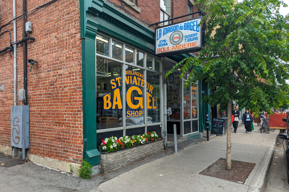 Exterior of St. Viateur Bagel Shop in Montreal, a renowned bakery known for its hand-rolled bagels, with a bright sign, large windows, and flower boxes under a brick facade.