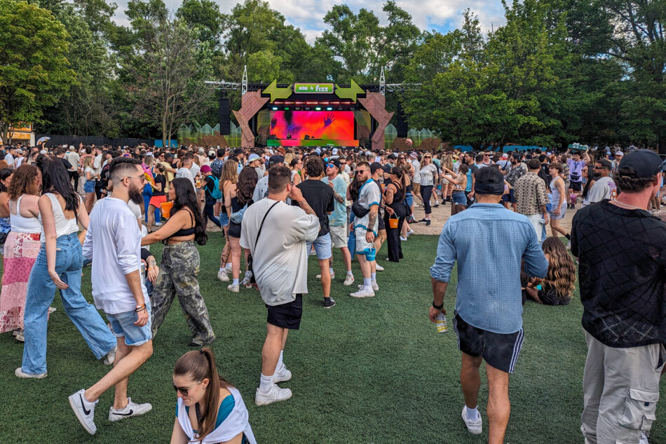 Vibrant scene at Piknic Electronik in Montreal with a diverse crowd of attendees enjoying the outdoor music festival, with a large stage displaying vivid graphics in the background.