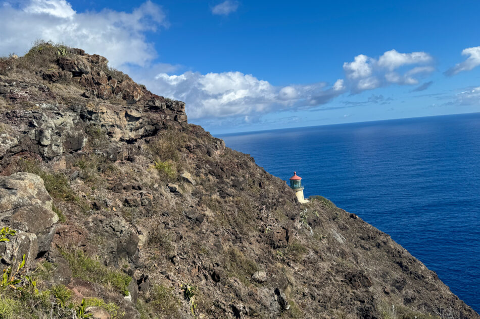 The historic Makapuʻu Point Lighthouse perched on a rugged cliff, surrounded by rocky terrain and overlooking the deep blue expanse of the Pacific Ocean.